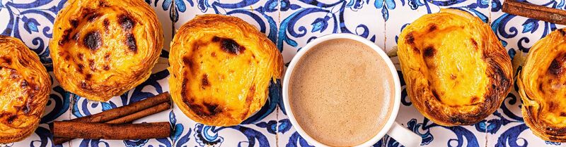 Delicious pasteis de nata from Lisbon's Belem neighborhood, accompanied by coffee on a table with traditional white and blue tiles.