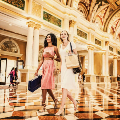 Two smiling women walking and carrying shopping bags in a luxurious shopping mall with opulent decor