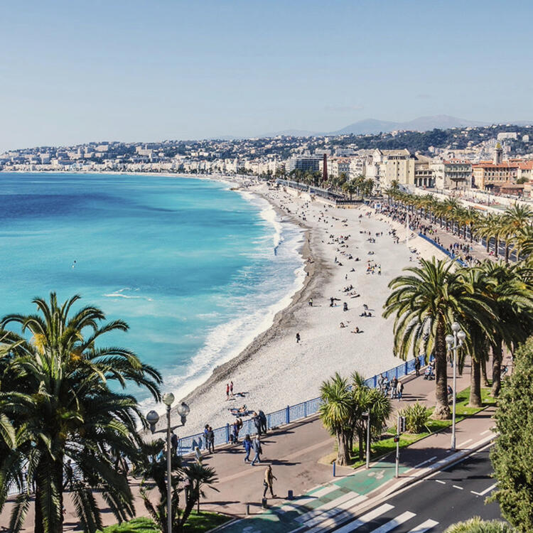 Scenic view of the Promenade des Anglais along the picturesque coastline of Nice, France, with azure waters, pebble beach, and lined with palm trees under a clear blue sk