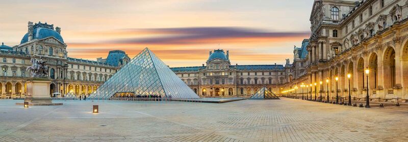 Paris (CDG) Stunning panorama of the Louvre Museum courtyard at dusk, showcasing its iconic glass pyramids, majestic historic architecture, and a captivating gradient sky with hues of pink and orange.
