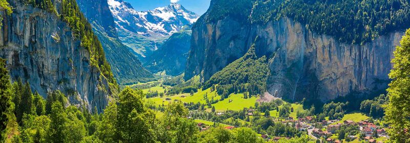 View of the Lauterbrunne Valley, in Switzerland. The lush valley unfolds beneath towering mountain peaks, offering a vibrant tapestry of greenery cradled in an alpine embrace, illuminated by the soft light of the sun.