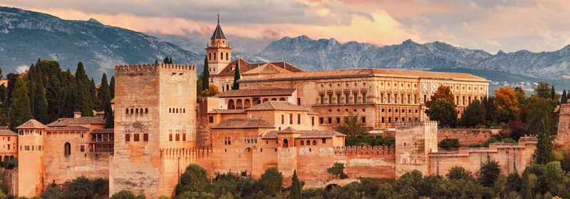 Flights to Malaga (AGP) Alhambra fortress in Granada, Spain, bathed in warm sunlight with backdrop of cloudy blue skies and distant mountains.