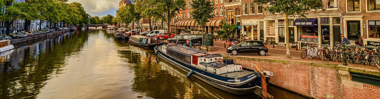 A picturesque canal in a European city with moored boats, lined by historic buildings, bicycles parked along the side, and a sign for canal tours.