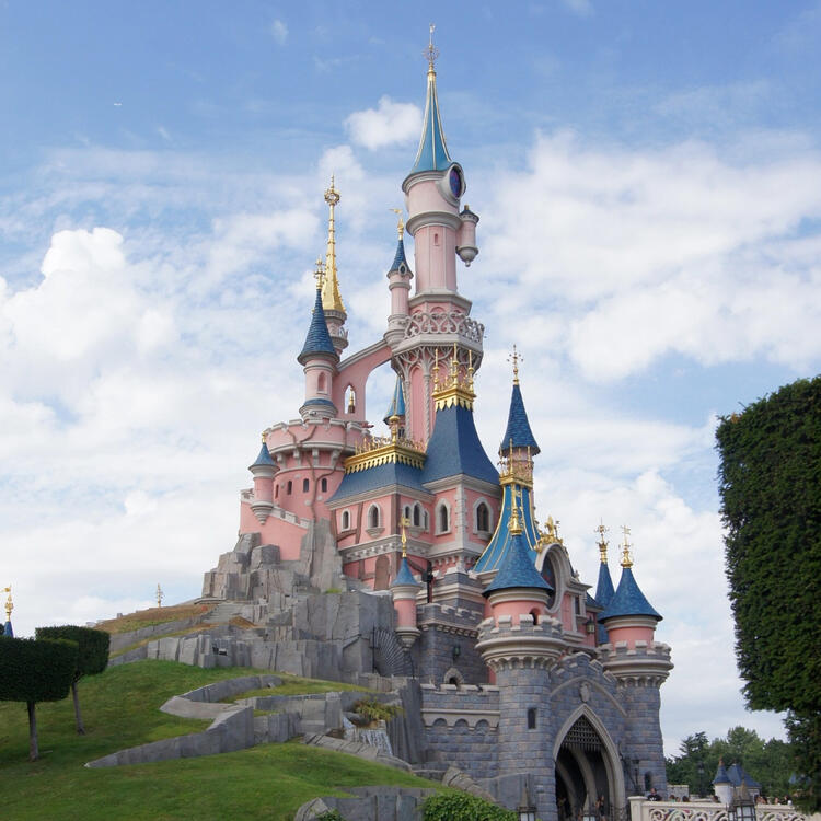 A fairytale castle with pink and blue turrets under a blue sky with fluffy clouds.